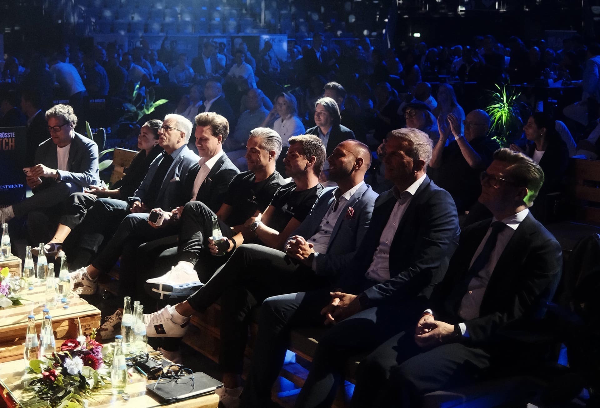 Investoren und Unternehmer sitzen in der ersten Reihe und verfolgen einen Pitch auf der Bühne.