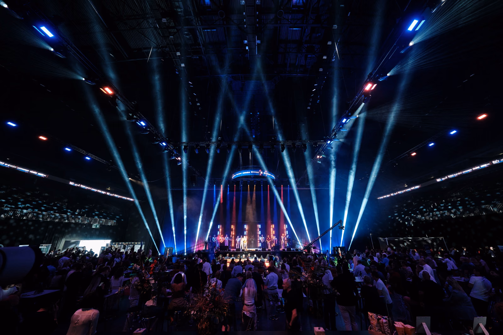 Volle LANXESS arena von oben: Lichtstrahlen fächern über das Publikum bis unter das Hallendach.