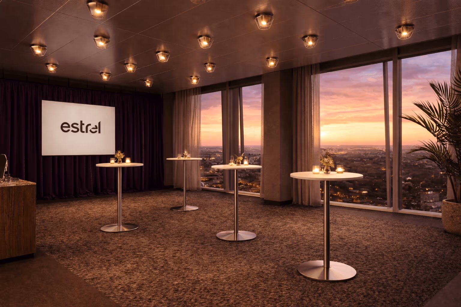 Der Sky-Space-Eventraum im Estrel Berlin: Stehtische vor der Panoramafront, Sonnenuntergang über der Stadt, das estrel-Logo auf der Bühnenleinwand.