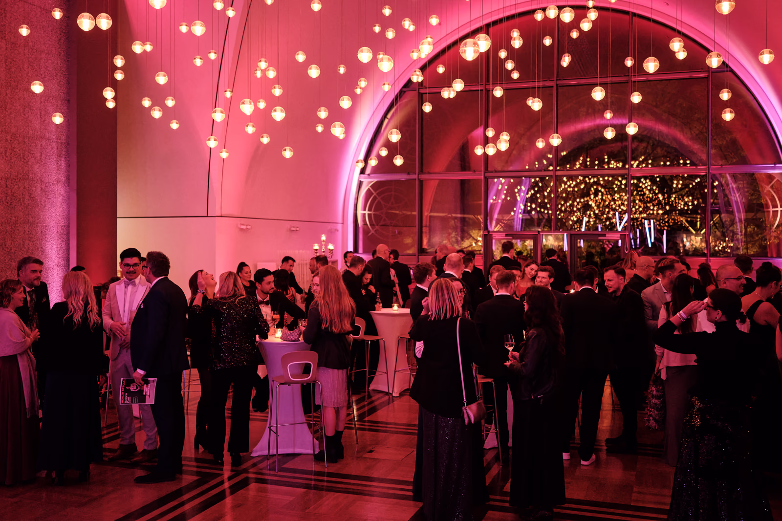 Gäste stehen im pink ausgeleuchteten Foyer der Flora an Stehtischen zusammen.