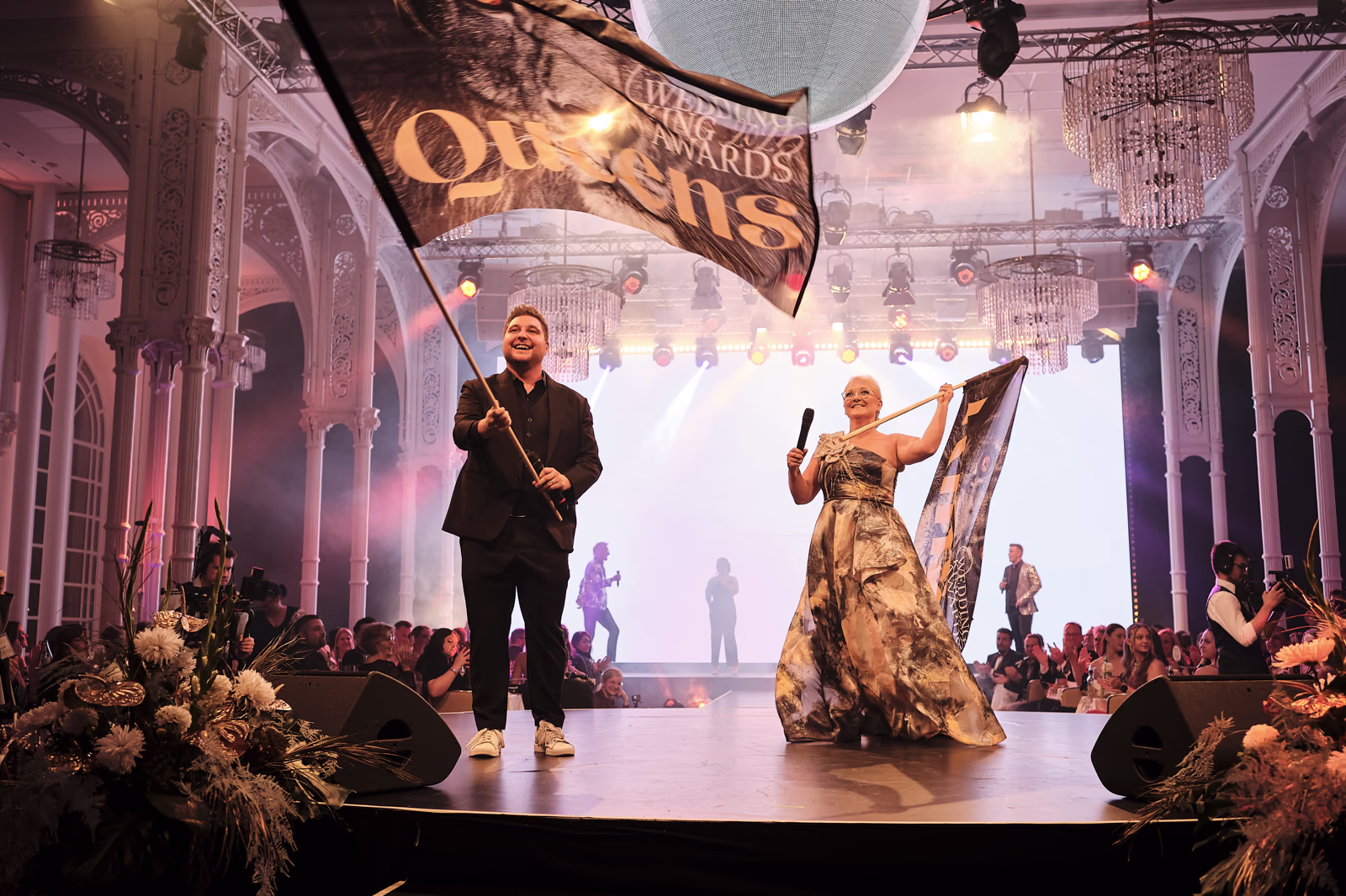 Wedding King Awards: Moderationsduo mit wehenden Fahnen auf dem Laufsteg.